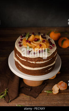 The chocolate cake with clementines, cranberry and rosemary on cakestand wooden background. Still life. Stock Photo