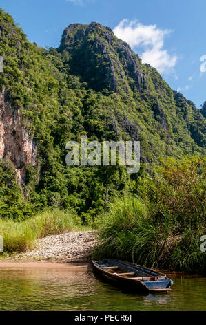Wooden boat moored on the bank of a river in a very quiet place under the mountains, Vang Vieng, Laos Stock Photo