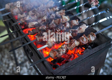 Shashlik preparing on a barbecue grill over charcoal. Pieces of meat on skewers. Shish kebab prepare on fire. Stock Photo