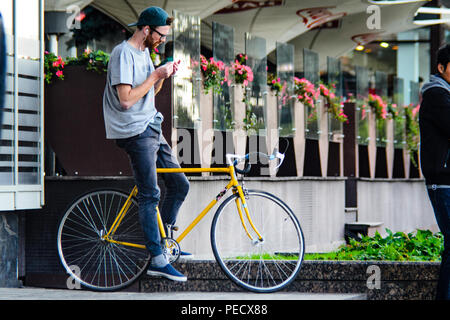 September 22, 2018 Minsk, Belarus: Young man stand with yellow fixie bike in cityscape and makes hand-roll cigarette Stock Photo