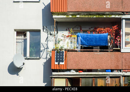 Facade of a residential high-rise building: a cluttered balcony with a homemade solar battery, antennas and a satellite dish Stock Photo