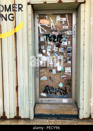 A glass door on a metal building covered in stickers and graffiti Stock Photo