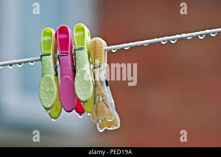 Four clothes pegs hang forlornly on a dripping wet washing line Stock Photo