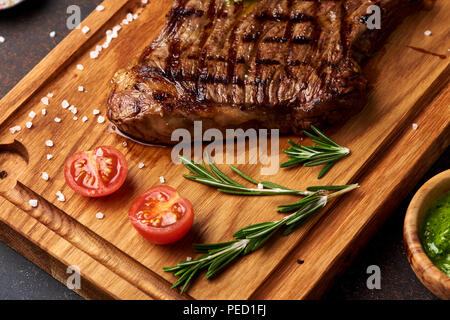 Grilled Black Angus Steak with tomatoes, garlic with rosemary on meat cutting board. Stock Photo