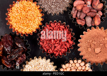 Various superfoods in small bowl on blackbackground. Superfood as chia, raw cocoa bean, goji, chickpeas, lentils. Copy space. Flat lay. Stock Photo