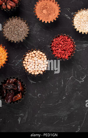 Various superfoods in small bowl on blackbackground. Superfood as chia, raw cocoa bean, goji, chickpeas, lentils. Copy space. Flat lay. Stock Photo