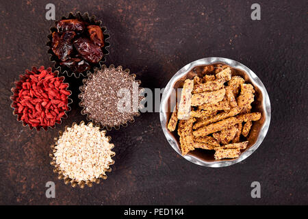 Various superfoods in small bowl near granola on black background. Superfood as chia, raw cocoa bean, goji, oatmeal. Copy space. Flat lay. Stock Photo