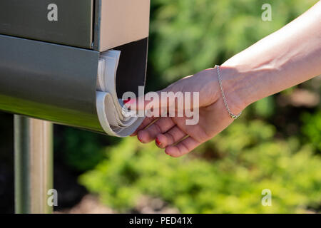A Woman takes the newspaper off a mailbox. Stock Photo