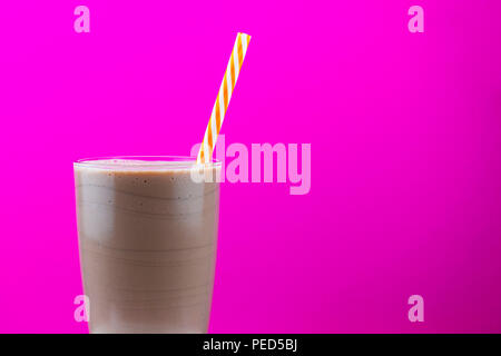Chocolate milkshake in a glass with a straw against a bright pink background with copy space Stock Photo