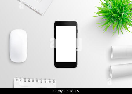 Black modern smart phone on white office desk surrounded with pad, plant, project papers and computer mouse. Isolated, white, blank screen for mockup. Stock Photo