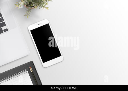 Phone mockup on office desk. Laptop computer, plant and pad beside. Flat lay. Top view. Stock Photo