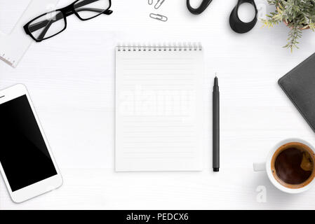 Blank notebook on office desk surrounded with pen, glasses, cup of coffee, mobile phone. Flat lay, top view. Stock Photo