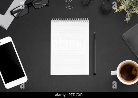 Notebook on black desk surrounded with office accessories. Blank paper, flat lay. Stock Photo