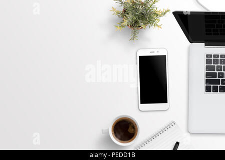 Phone and laptop computer on white desk with free space for text. Plant, cup of coffee, notepad nad pencil beside. Flat lay composition. Stock Photo