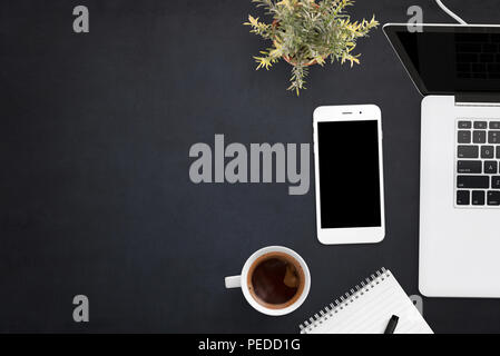 Smart phone and laptop on black office desk with copy space on left side. Blank screen on devices for mockup, app or web site presentation. Stock Photo