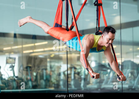 Fit handsome man smiling while practicing anti-gravity yoga Stock Photo