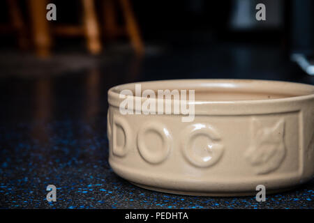 An empty large ceramic dog food bowl on a dark kitchen floor Stock Photo