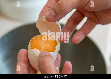 Female hands separate the egg white from the yolk over a bowl in the kitchen. the cook separates the yolk in the egg. Stock Photo