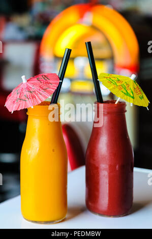 Two brightly coloured drinks with cocktail umbrellas in front of a jukebox Stock Photo