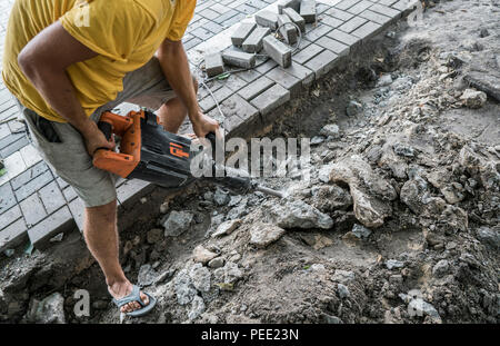 Workers use Electric Concrete Breaker. Male worker repairing driveway surface with jackhammer, digging and drilling concrete roads during sidewalk construction works Stock Photo
