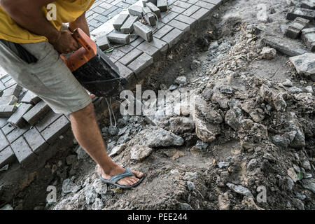 Workers use Electric Concrete Breaker. Male worker repairing driveway surface with jackhammer, digging and drilling concrete roads during sidewalk construction works Stock Photo