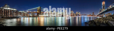 The skyscrapers of Lower Manhattan, the Brooklyn Bridge and the Manhattan Bridge in evening with the East River (panoramic). New York City Stock Photo