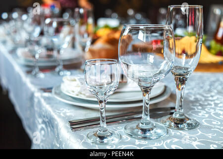 Serving of a festive table with a glass of wine glasses and a glass, and also plates with napkins on a white tablecloth Stock Photo