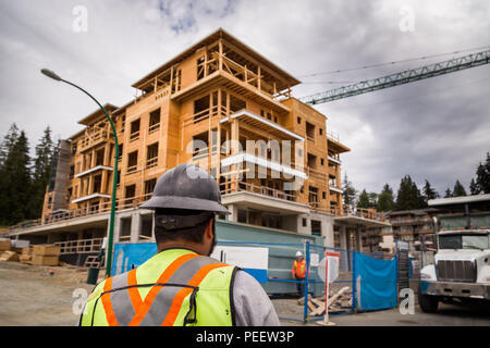 Construction worker in a hardhat observes an apartment complex under construction. Stock Photo