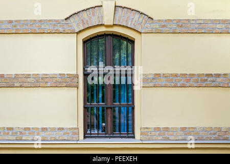 Window with arch and iron bars on the yellow wall with decorative strips of brick. Stock Photo