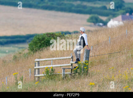 A man sitting on a fence looking out at the view from the Devil's Dyke on the South Downs in East Sussex, England, UK. Stock Photo