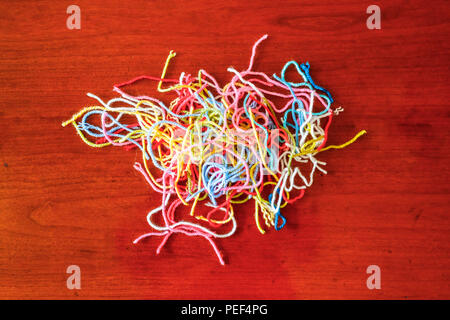 Abstract pattern: Colourful pile of left over lengths of pastel brightly coloured strands of wool offcuts used for home handicrafts on a wooden table Stock Photo