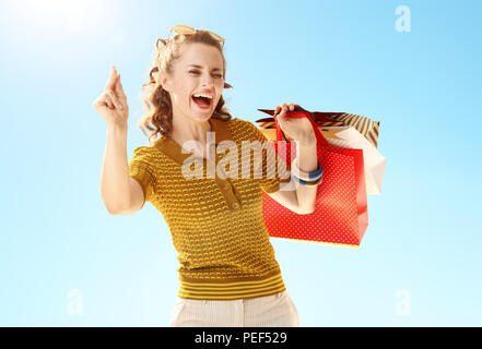 smiling young woman with shopping bags fingers snapping against blue sky Stock Photo