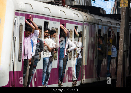 Passengers hanging out of trains door on a Mumbai Suburban Railway train at Bandra station in Mumbai, India Stock Photo