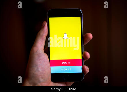Hand holding iPhone with Snapchat App, login screen, social network, instant messenger, app icon, iPhone, iOS, smartphone Stock Photo