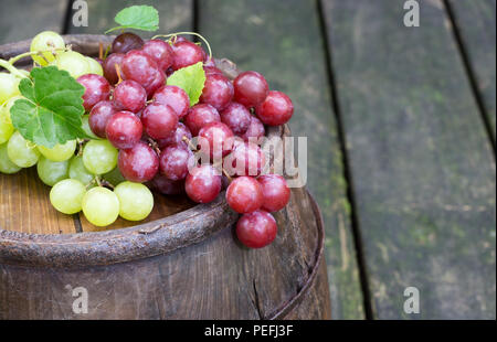 Fresh red and green grapes on top of an old wine barrel on a rustic wooden surface Stock Photo