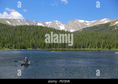 Fisherman rowing on a boat on Brainard lake in Colorado with the Rocky Mountains of the Indian Peaks in the background Stock Photo