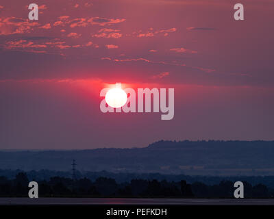 Red, pink and purple sunrise with the sun over an urban area. Pollution from smoke from forest fires makes a dramatic sunrise. Stock Photo