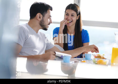 Young hispanic couple having breakfast together on Sunday morning, sitting at table and eating organic food. They smile and eat Stock Photo