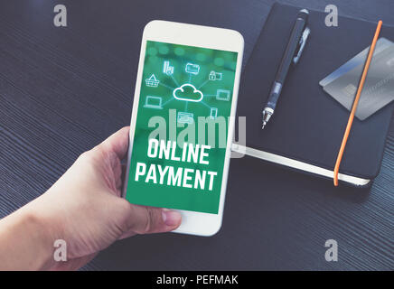 Hand holding mobile talking with online payment on screen with black notebook and credit card on black wooden desk,Digital marketing technology concep Stock Photo
