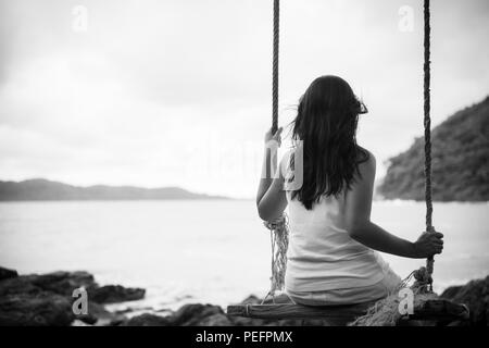 Black and white of Sad and lonely woman sitting alone on a the wooden swing over the sea