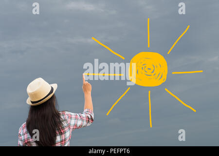 Woman drawing or painting sun onto grey sky. need sun light. change concept. Stock Photo