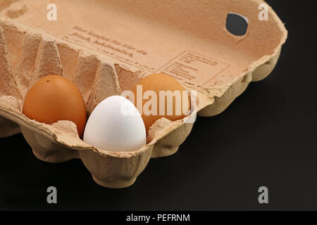Three Brown Eggs In A Grey Cardboard Box on black background Stock Photo
