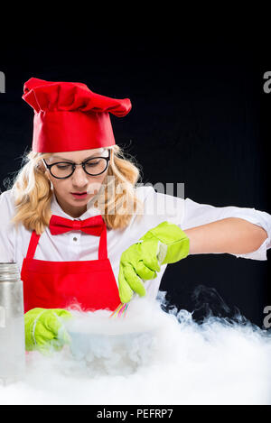 Woman animator cook doing experiments with liquid nitrogen, portrait on black background Stock Photo