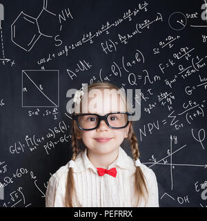 Little genius. Smart little girl math student on school blackboard background with hand drawings science formula pattern. Kids mathematics education c Stock Photo