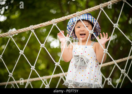 Happy little girl playing climbing on the rope bridge in adventure park colorful garden on hot summer day. Summer activities for kids. Stock Photo