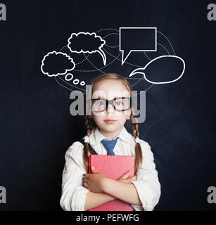 Pretty little girl holding book and standing against speech clouds chalk drawing on blackboard background Stock Photo