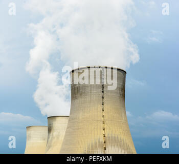 Three natural draft cooling towers of a nuclear power plant releasing clouds of water vapor against a dark stormy sky. Stock Photo