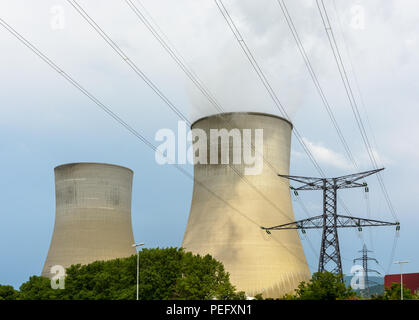 Two cooling towers of a nuclear power plant releasing clouds of water vapor with a transmission tower supporting a high voltage overhead power line in Stock Photo