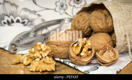 Horizontal photo of walnut shells and walnut kernels bursting out of burlap sack on top of marble surface with white towel with flowers. Stock Photo