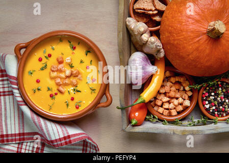 Pumpkin soup in ceramic bowl on light wood served with thyme and croutons. Next to it is a tray with healthy soup ingredients. Flat lay, view from abo Stock Photo